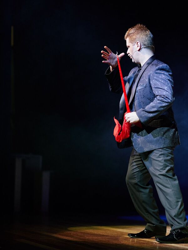 John Messina performing on stage with red silk and dramatic blue stage lighting